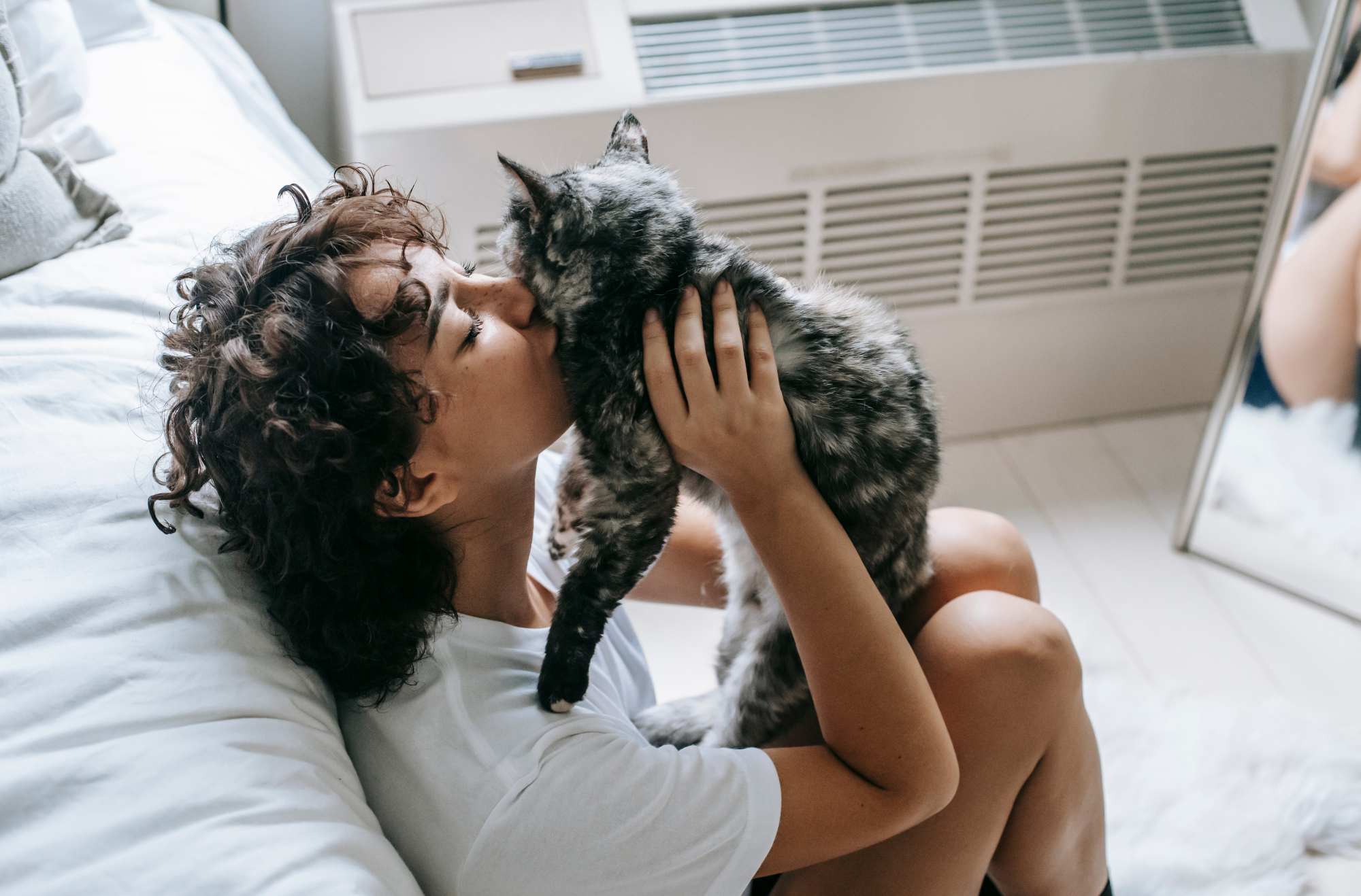 Beautiful brown haired woman kissing her calico cat. 