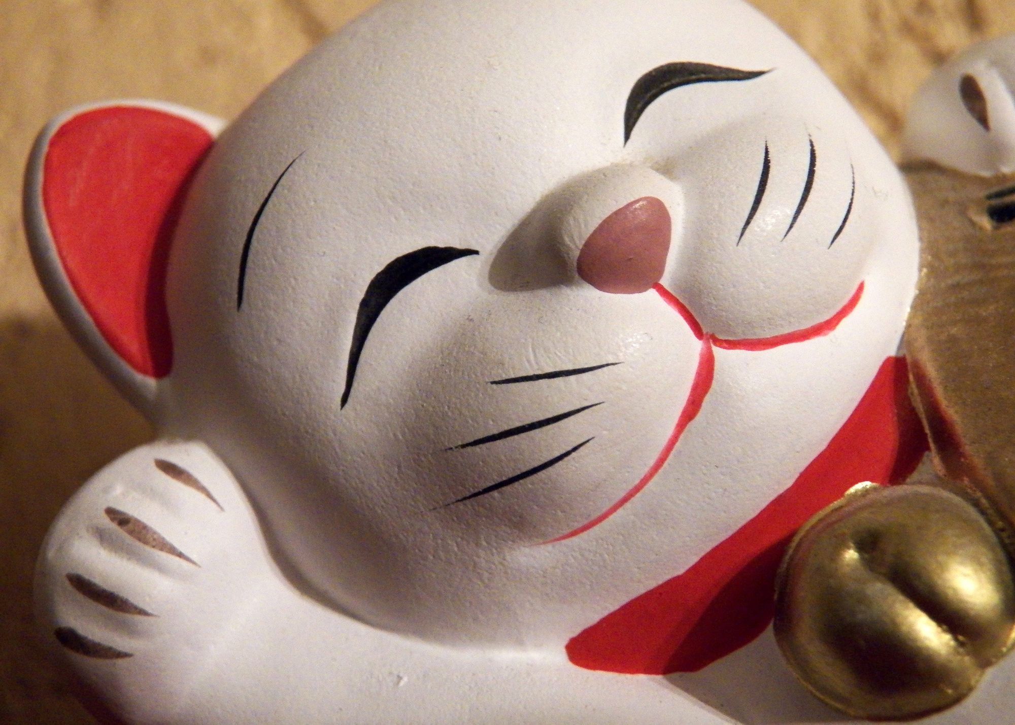 White lucky cat wearing a red collar with a gold bell. 